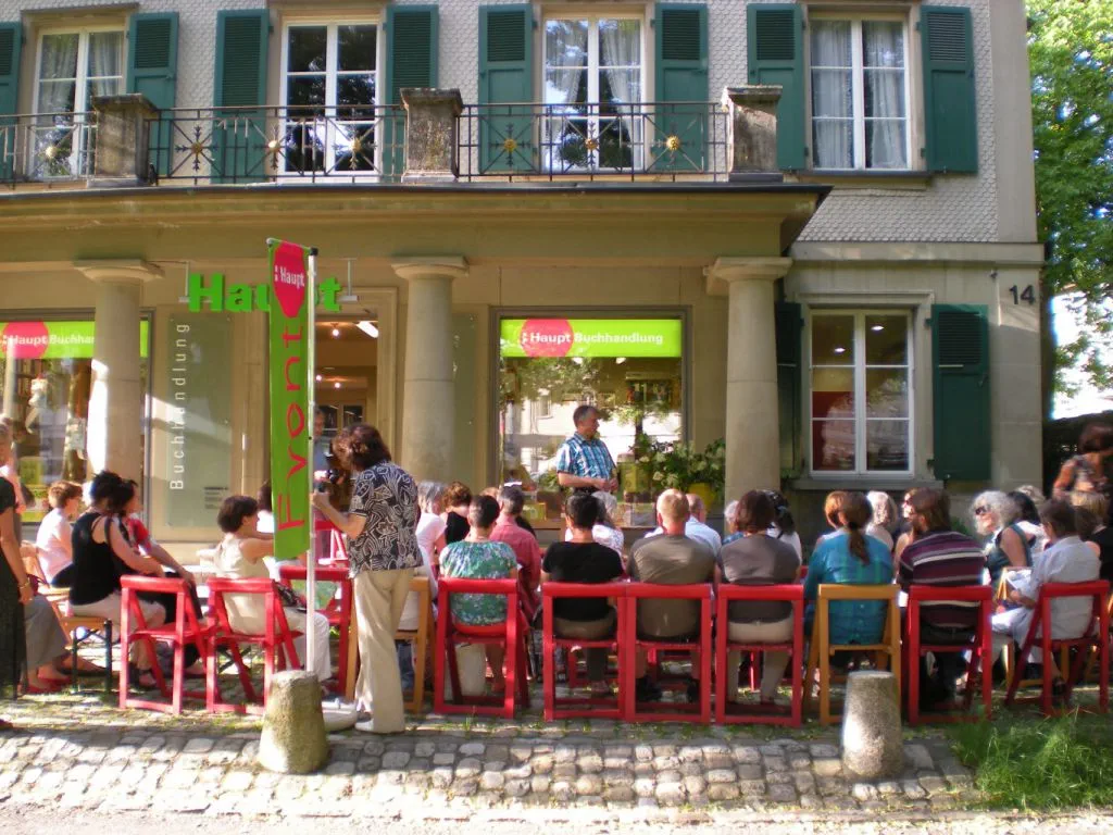 Gäste einer Buchvernissage auf Stühlen sitzend auf dem Vorplatz der Haupt Buchhandlung.