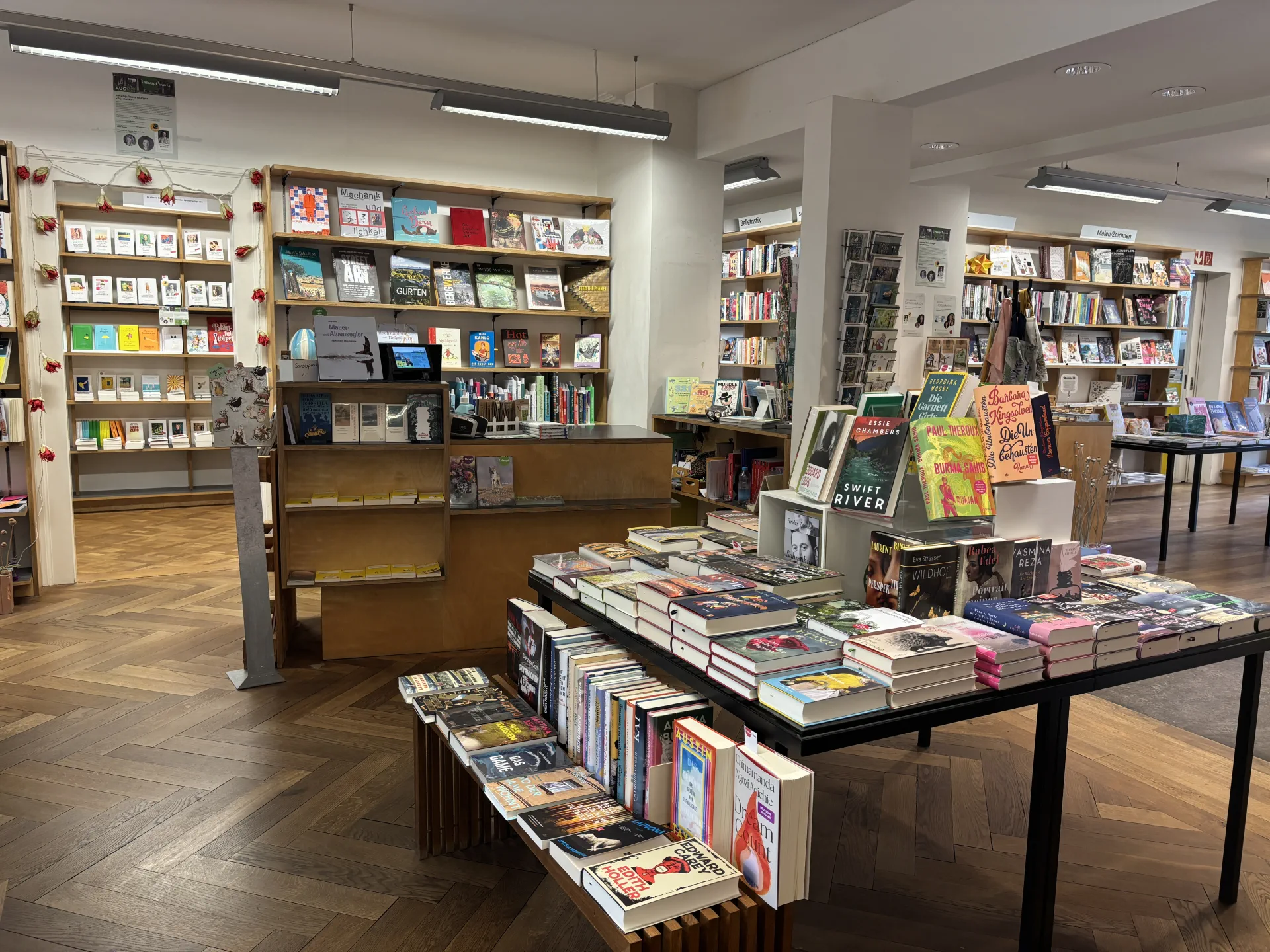 Innenansicht der Buchhandlung mit Theke, Büchertischen und Bücherregalen.